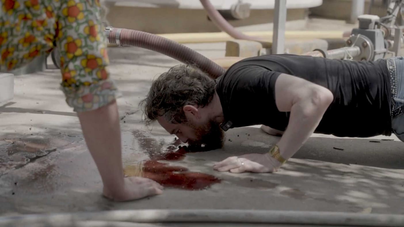 An image of Bobby Fingers, lying face down on the ground, tasting wine that has spilt on the floor of the d'Arenberg winery