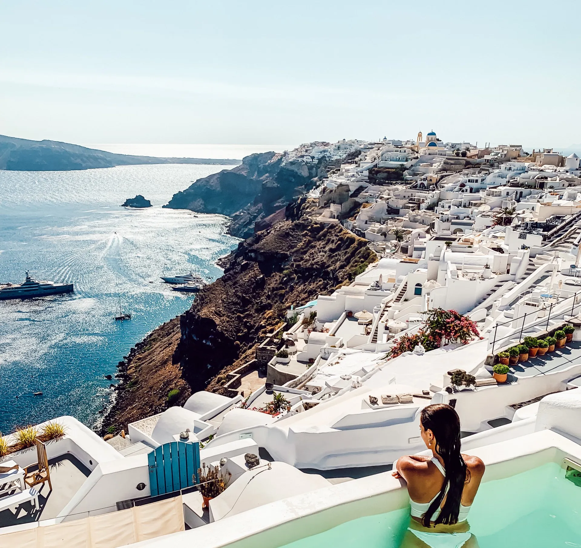 Frau im Infinity-Pool mit Blick auf Santorinis weiße Häuser und blaues Ägäis-Meer, Griechenland
