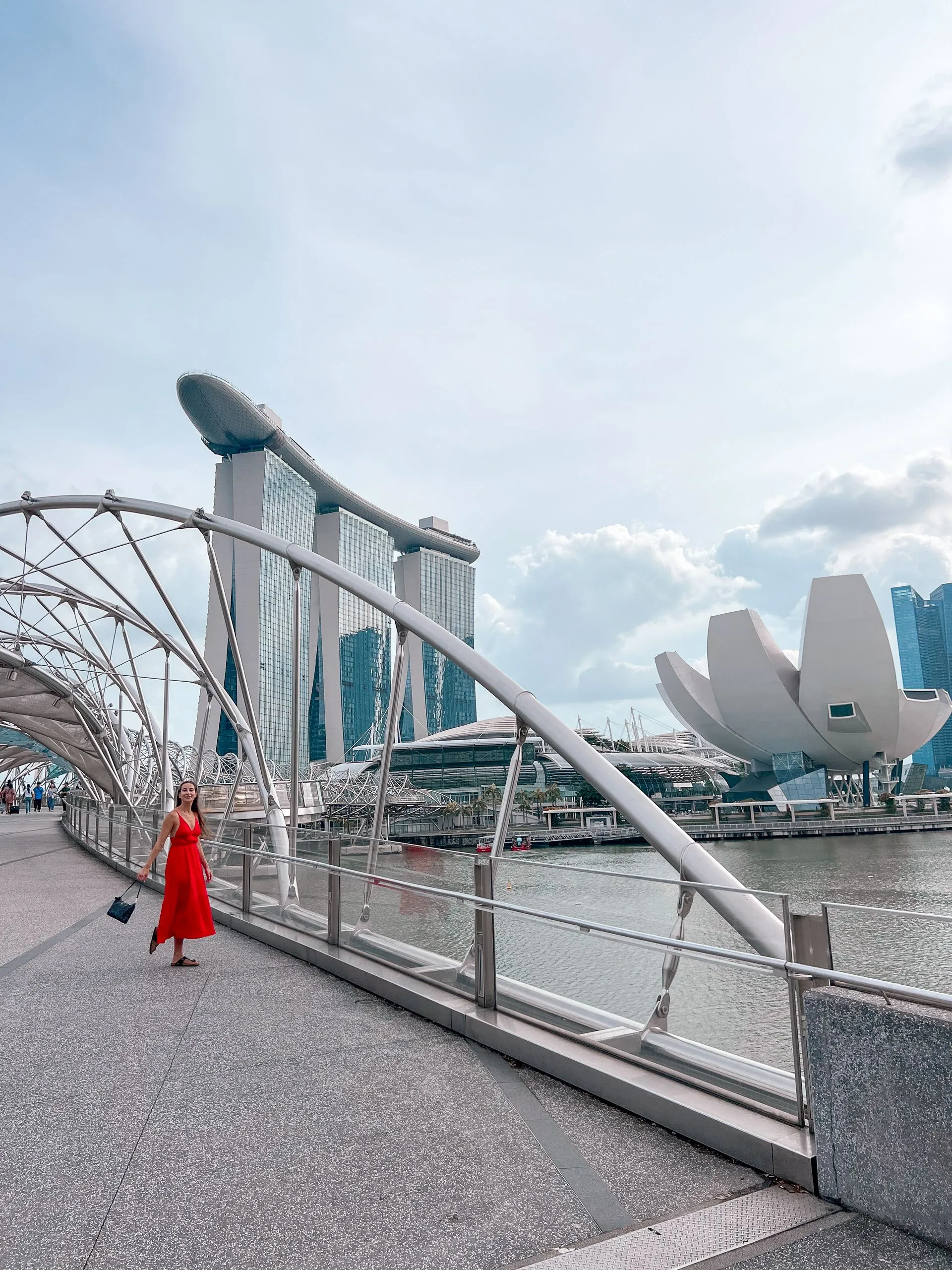 Frau im roten Kleid auf der Helix Bridge mit Marina Bay Sands und ArtScience Museum, Singapur
