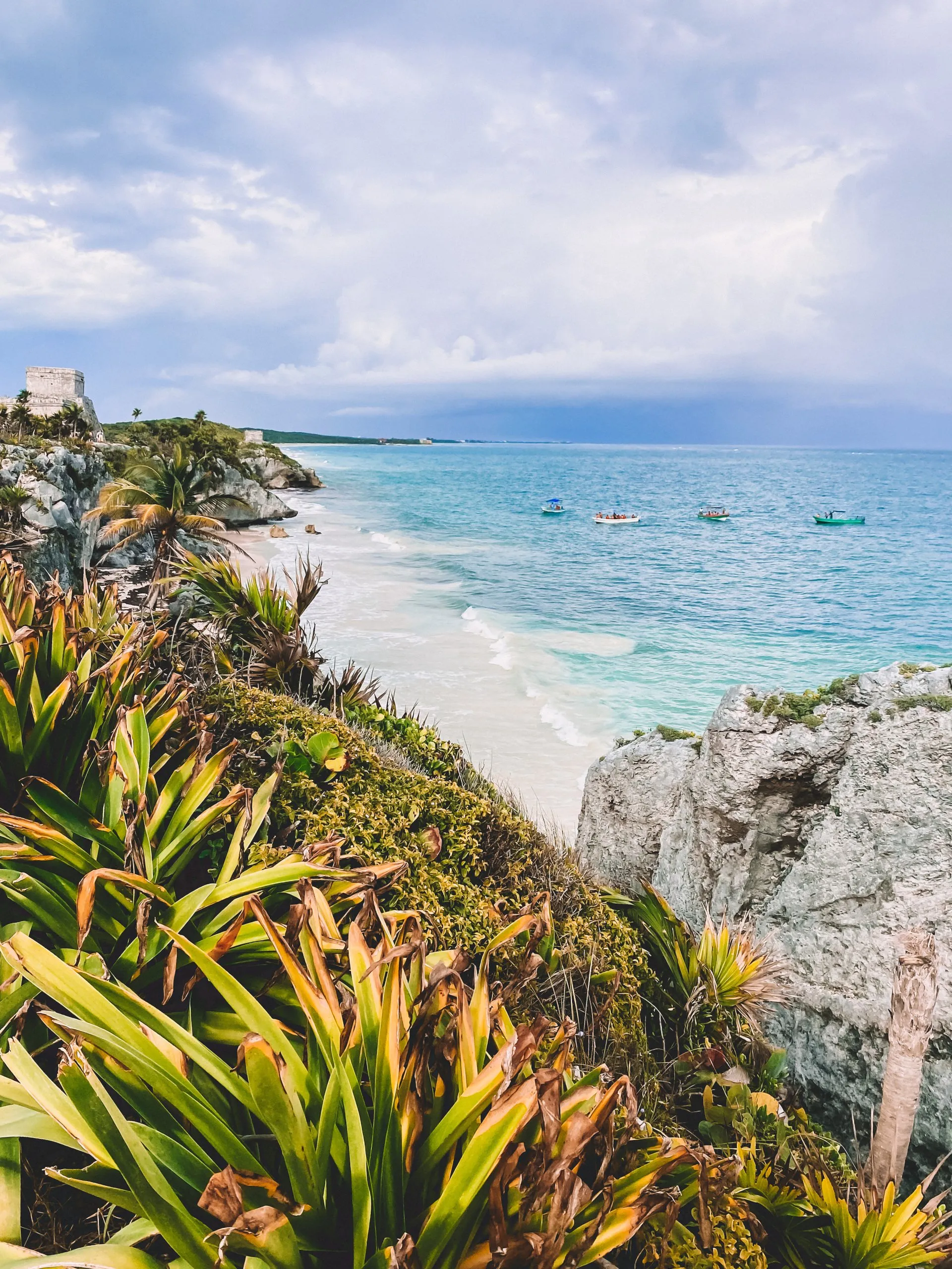 Blick auf den türkisfarbenen Strand von Tulum mit Maya-Ruinen, Klippen und Booten im Karibischen Meer, Mexiko.