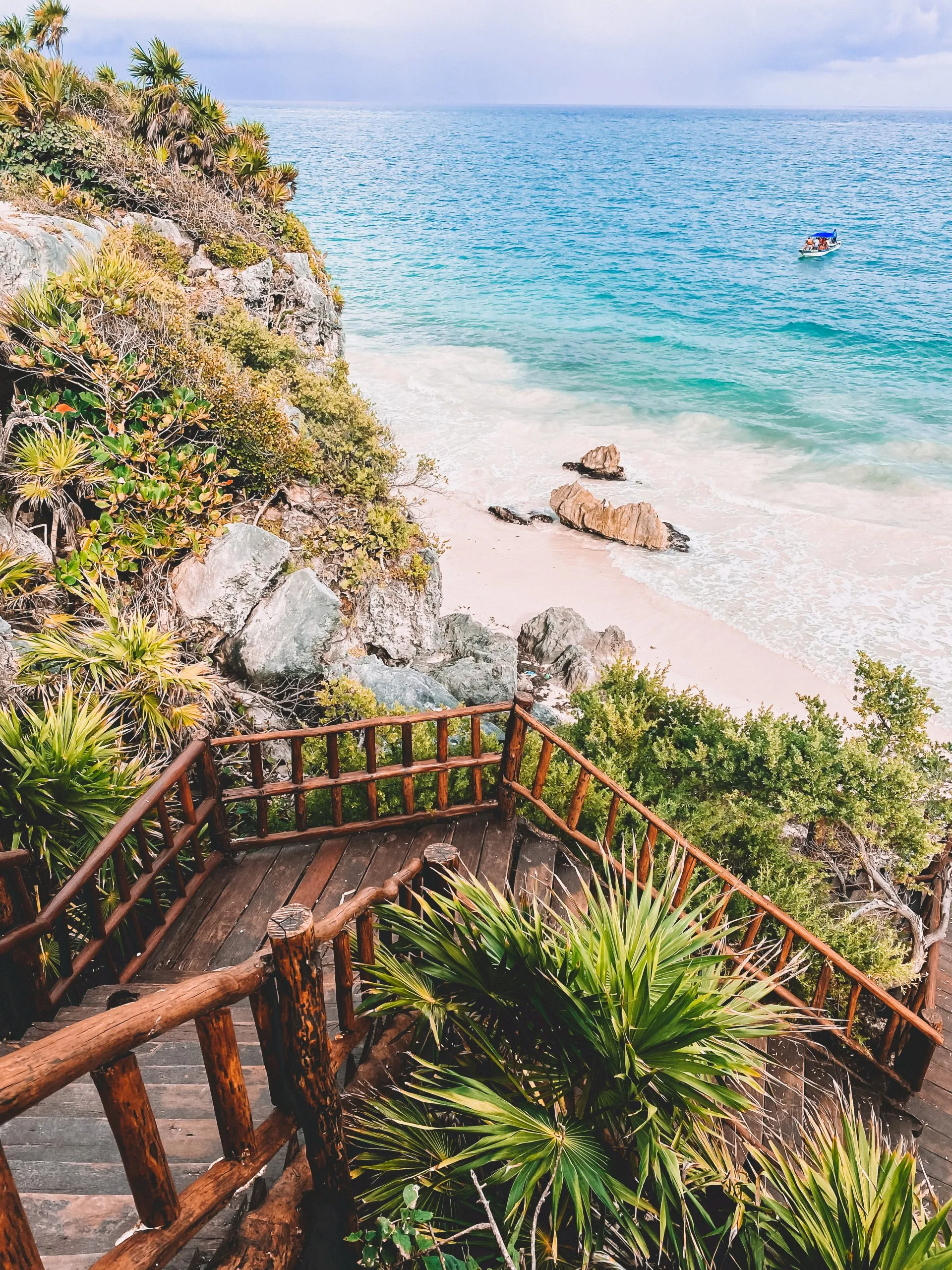 Holztreppe hinab zu weißem Sandstrand in Tulum, Mexiko, mit türkisblauem Karibikwasser und tropischer Vegetation