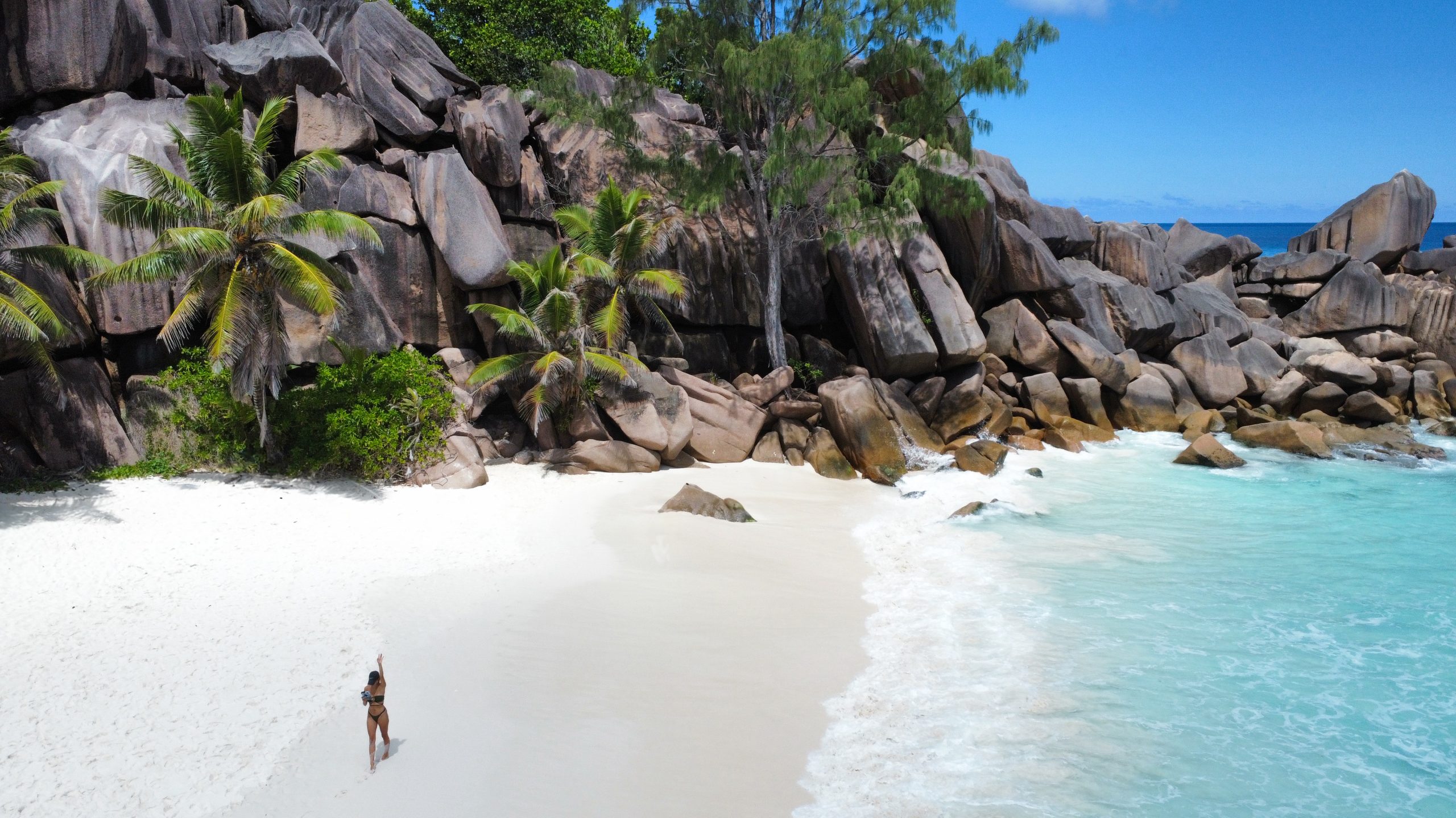 Frau am weißen Sandstrand der Seychellen mit türkisblauem Wasser und markanten Granitfelsen