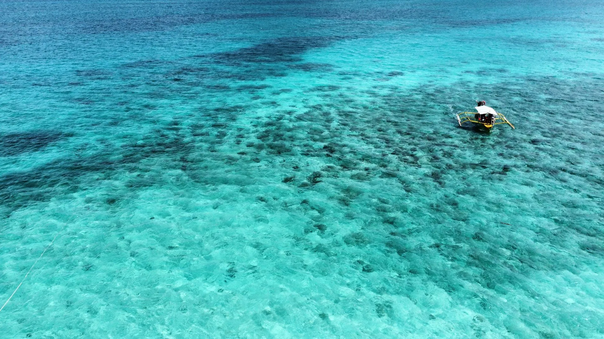 Türkisblaues Meer über Korallenriff mit traditionellem Bangka-Boot auf den Philippinen