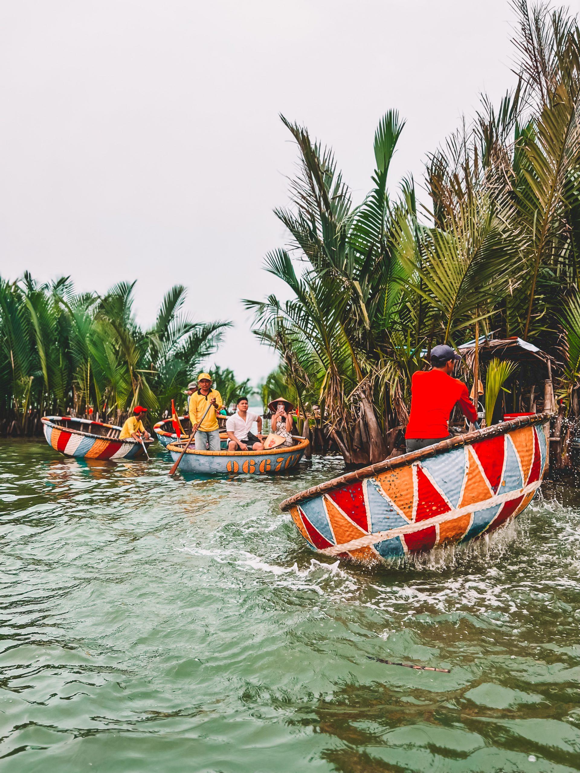 Bunte Korbboote auf dem Fluss in Hoi An, Vietnam, umgeben von tropischen Kokospalmen
