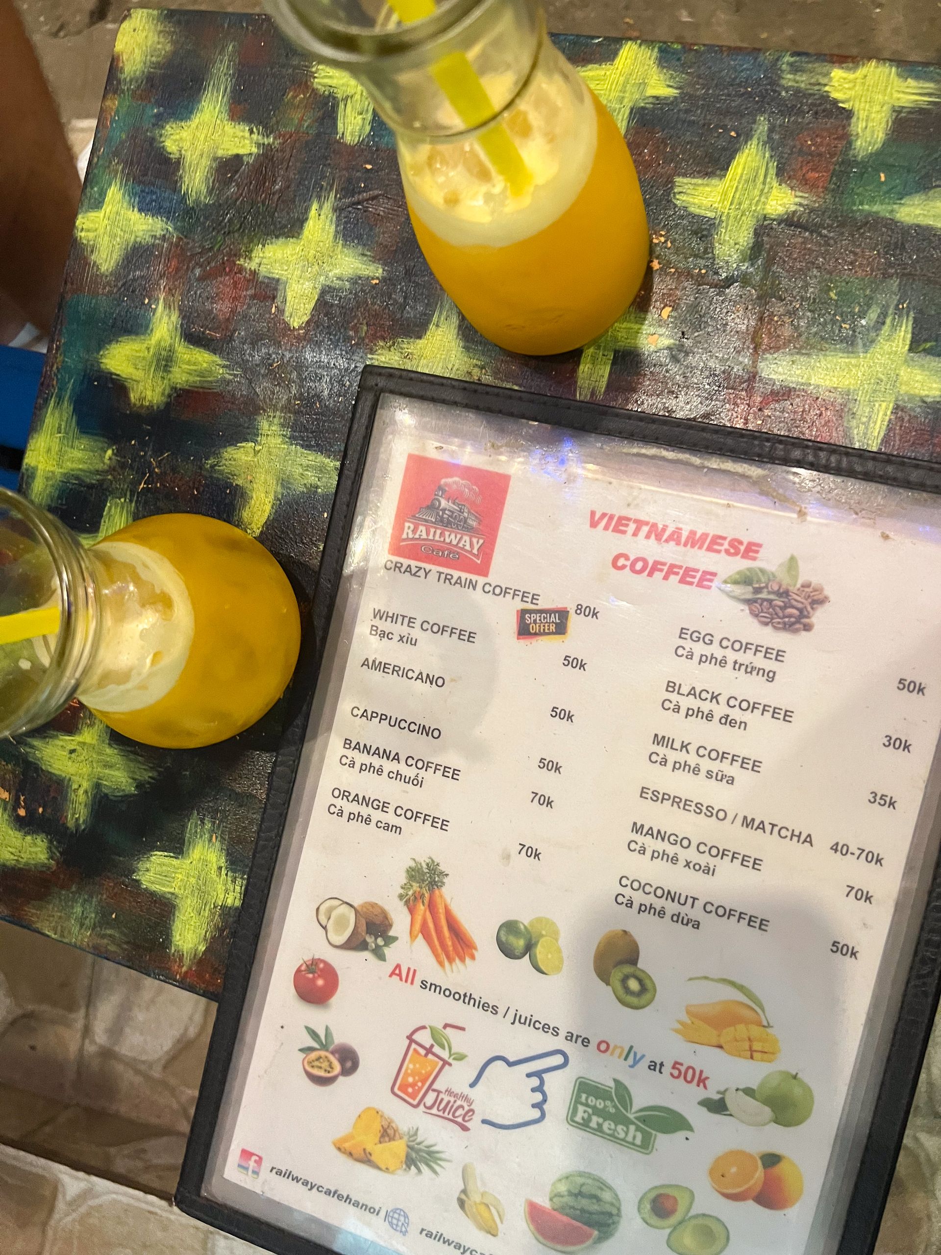 Menükarte des Railway Café Hanoi mit vietnamesischem Kaffee und frischen Säften auf buntem Tisch