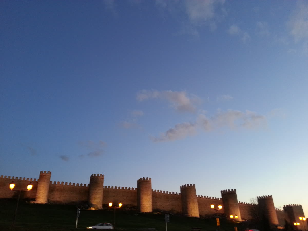 La muralla medieval de Ávila iluminada al atardecer, con sus torreones recortados contra el cielo