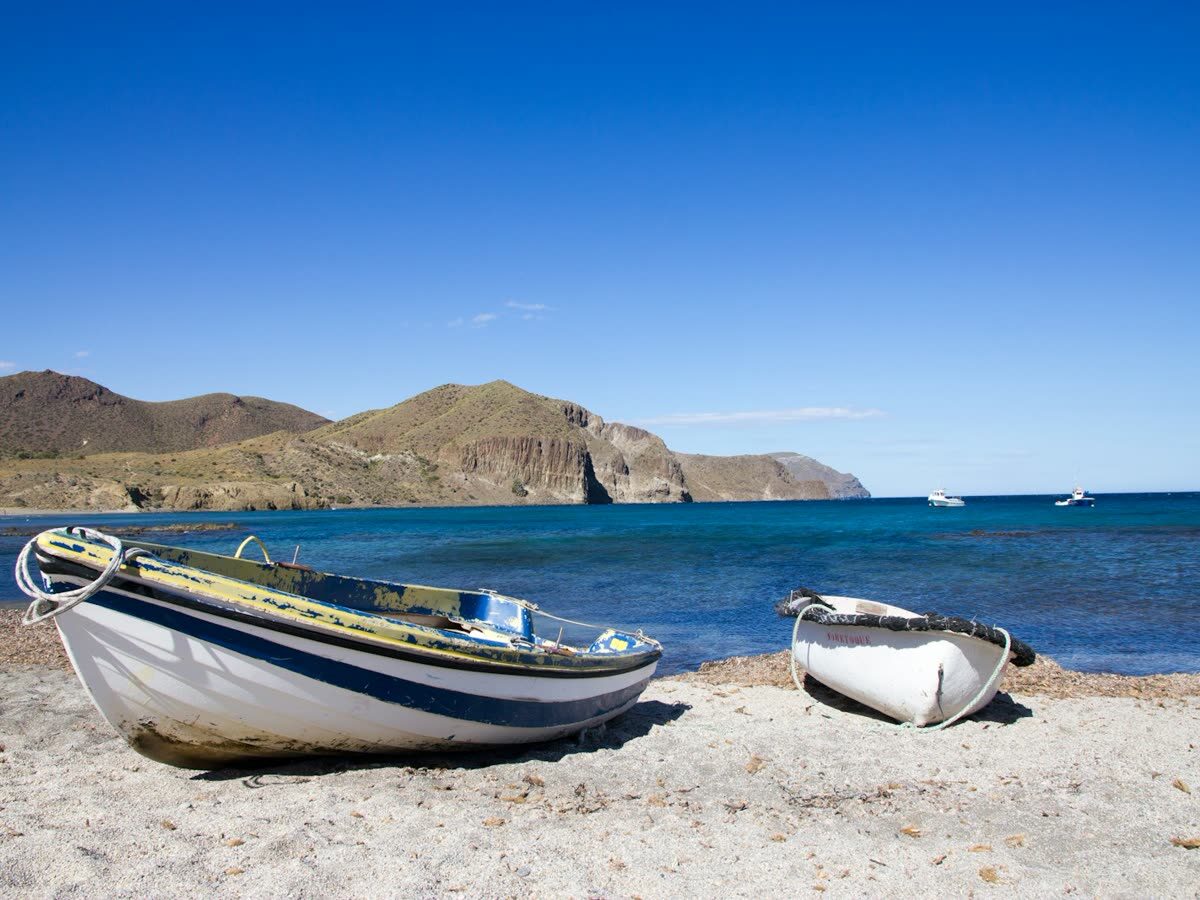 Barcas de pesca varadas en una cala de Cabo de Gata con acantilados volcánicos al fondo