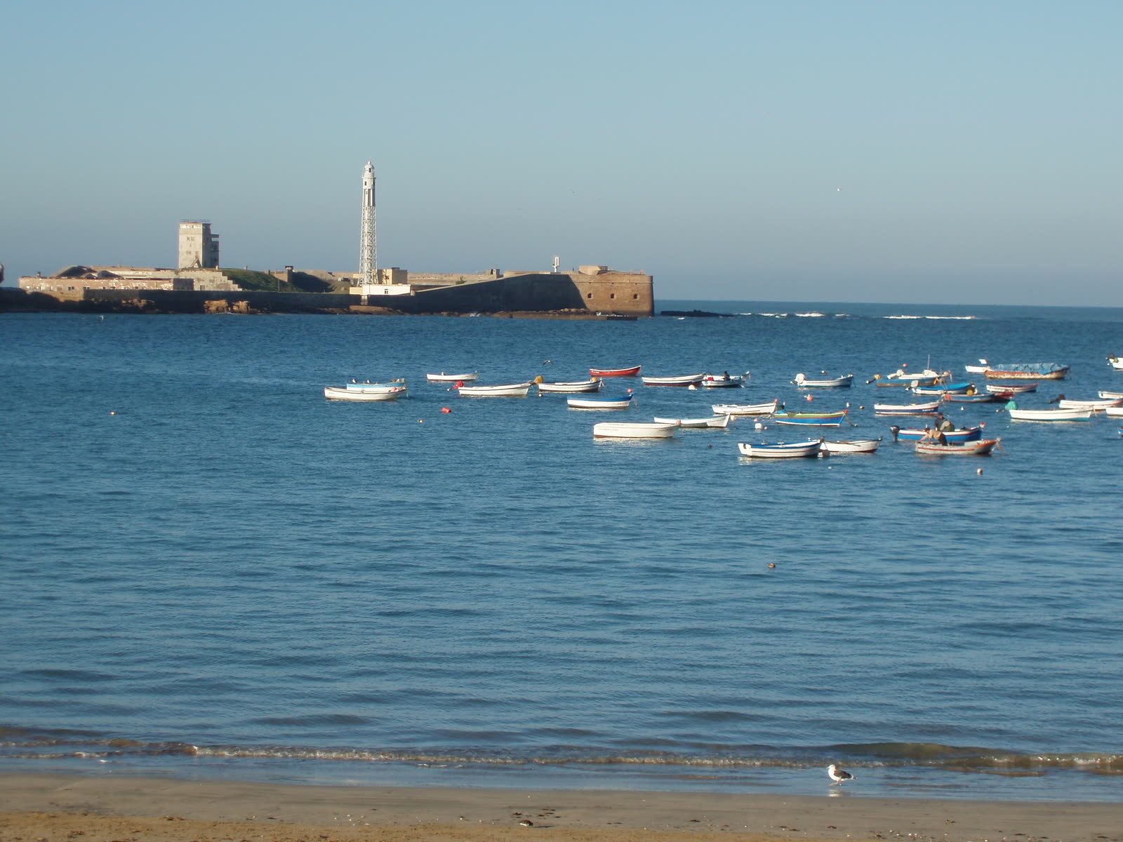 Playa de La Caleta en Cádiz con barcas varadas en la orilla y el Castillo de San Sebastián al fondo, en la bahía