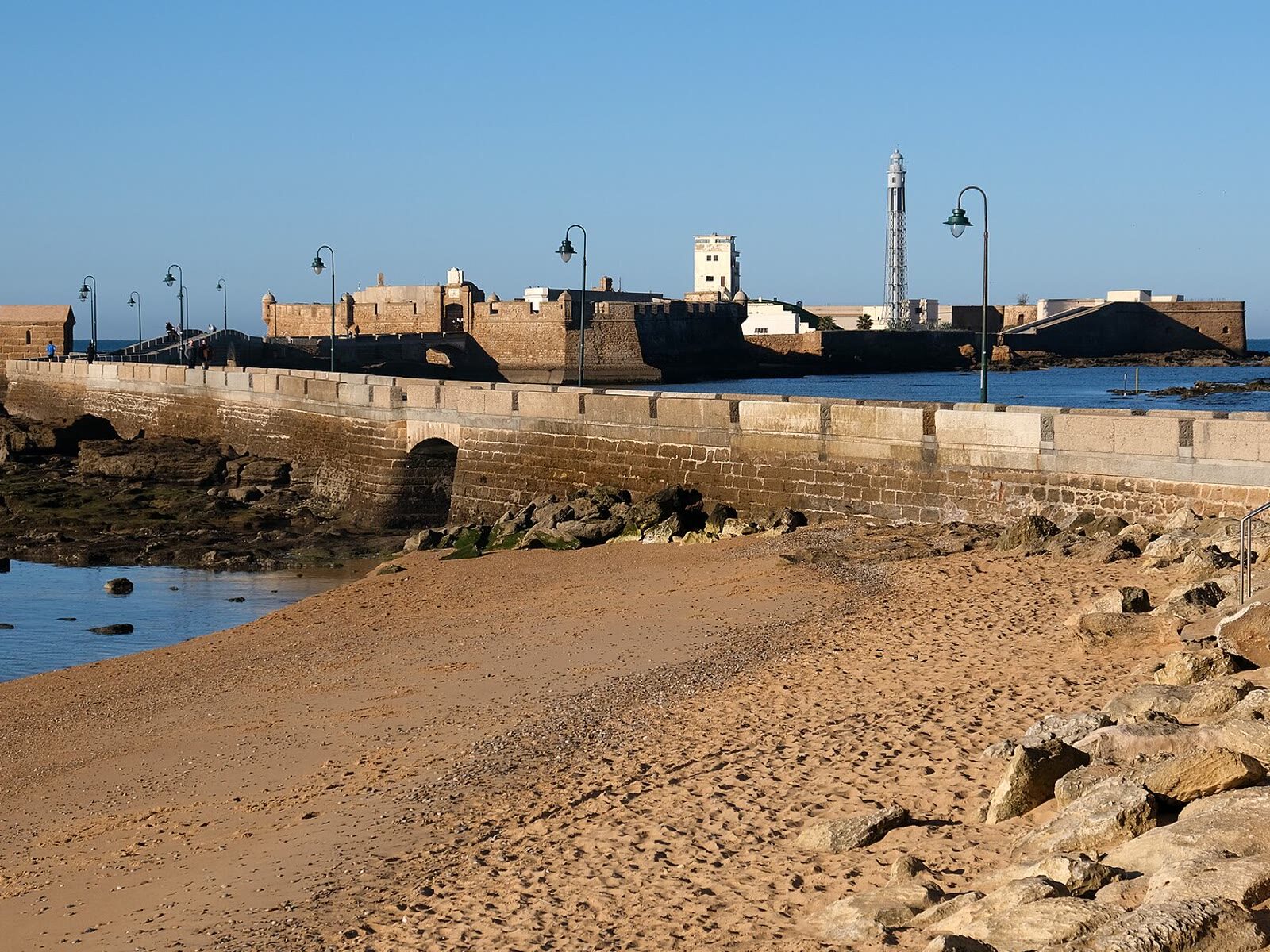 Paseo sobre el muelle hacia el Castillo de San Sebastián en Cádiz, con el faro al fondo