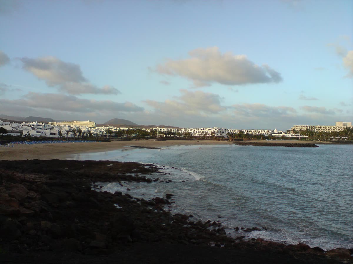 Bahía de Costa Teguise con la costa volcánica en primer plano y el desarrollo hotelero al fondo