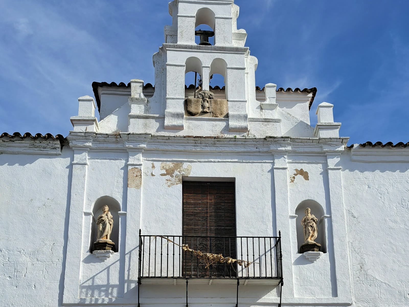 Fachada blanca de una iglesia extremeña con campanario y arco de acceso al pueblo
