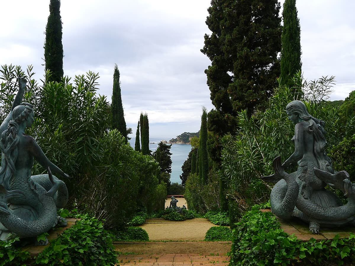 Estatuas de sirenas entre cipreses de los Jardines de Santa Clotilde con el mar al fondo