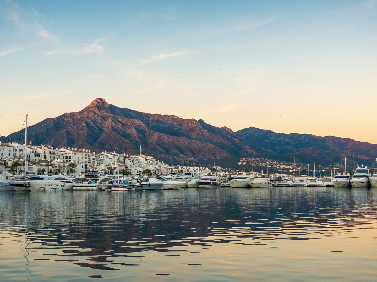Vista del puerto de Marbella al atardecer con embarcaciones y la montaña de La Concha al fondo