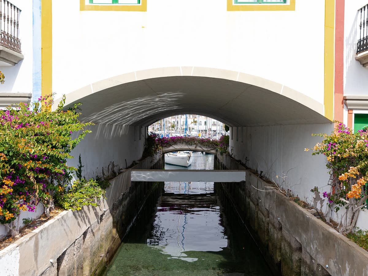 Canal de Puerto de Mogán bajo un puente encalado con buganvillas, la 'pequeña Venecia' canaria