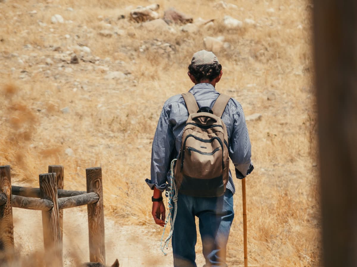 Senderista con mochila caminando por un sendero de tierra en un paisaje árido de montaña