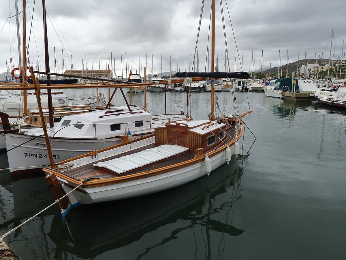 Embarcaciones amarradas en Port de Pollença, con el pueblo y la Serra de Tramuntana al fondo
