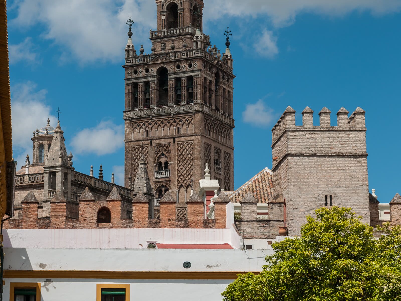 Vista de la Giralda y la Catedral de Sevilla desde los Reales Alcázares, entre las almenas y los tejados del casco histórico