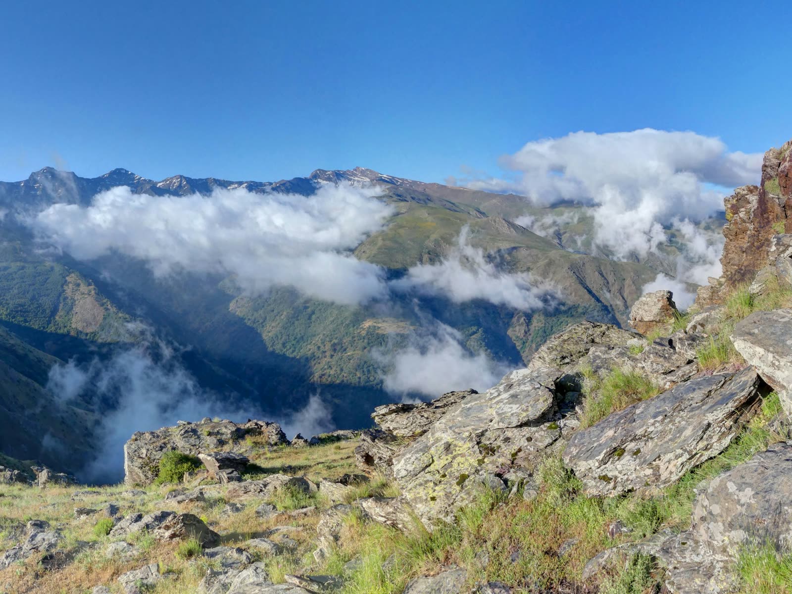 Cumbres de Sierra Nevada entre nubes vistas desde un mirador rocoso de alta montaña