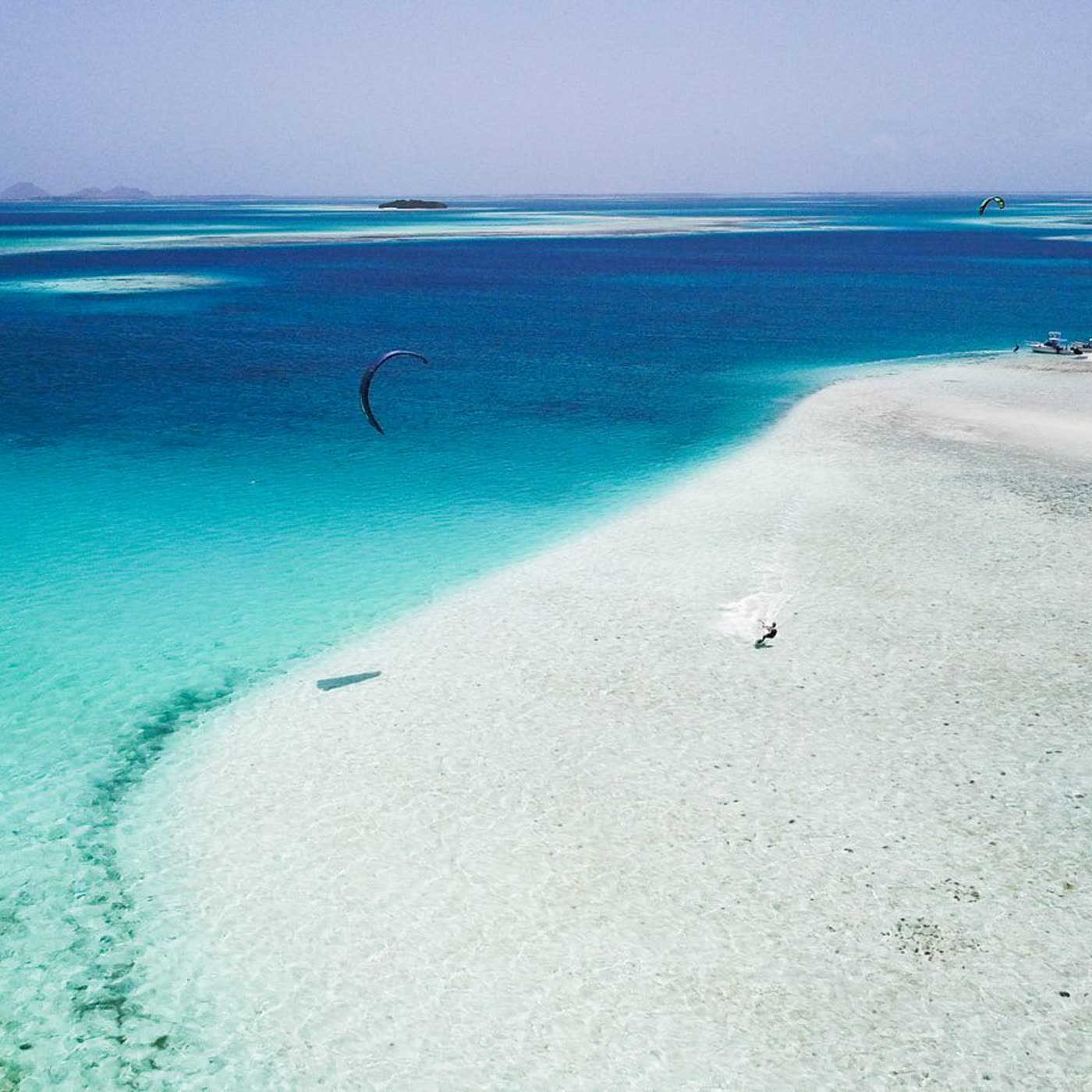 Vista aérea de un kitesurfista deslizándose junto a un banco de arena turquesa