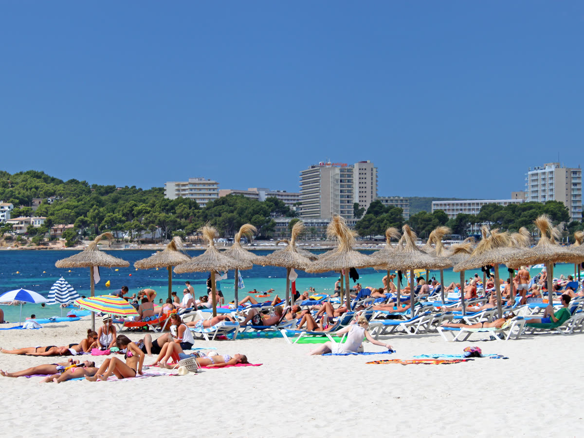 Playa de Magaluf con sombrillas de paja y la franja hotelera al fondo