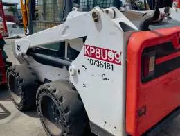 Bobcat S550 Skid_Steers A rear-side view of a Bobcat S550 skid steer loader. The loader has a white body with red accents on the rear panel. The tires are solid with a hole design around the edges, and the rear features visible identification numbers in red and black.