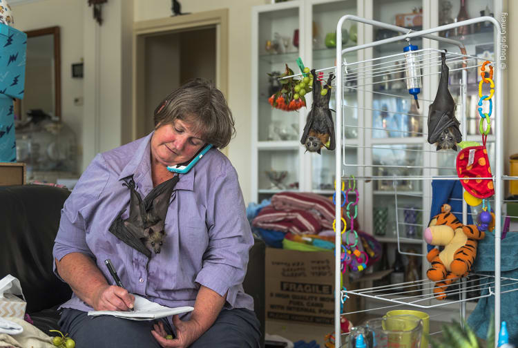 A woman on the phone with a bat hanging from her shirt.
