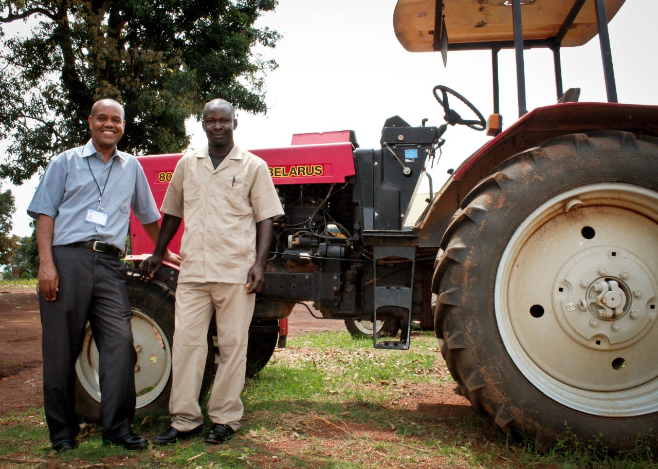 Two men smiling standing in front of a tractor.