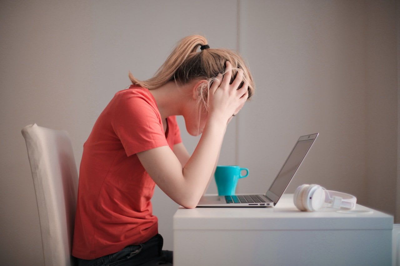 Woman siting at a table leaning forward looking at a laptop holding her head