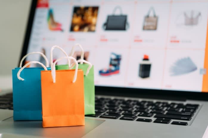 Miniature shopping bags on a laptop keyboard with an online shopping website in the background, symbolizing e-commerce and online shopping.