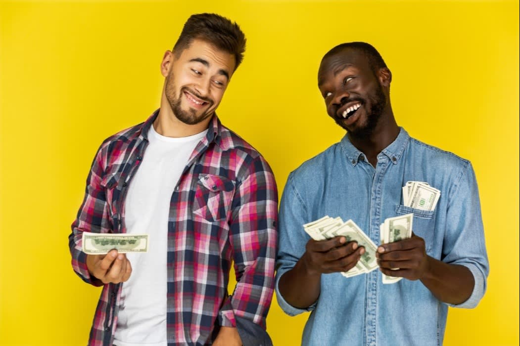 Two smiling men holding stacks of cash against a bright yellow background, symbolizing financial success and happiness.