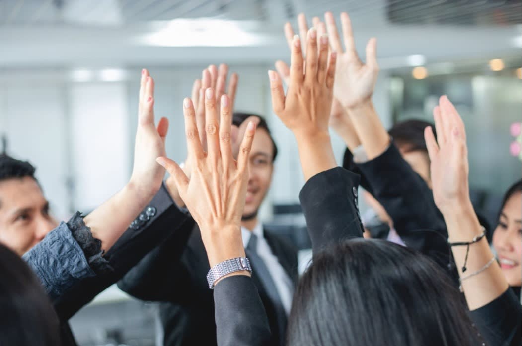 A group of professionals giving a high-five in an office, symbolizing teamwork, collaboration, and corporate success.