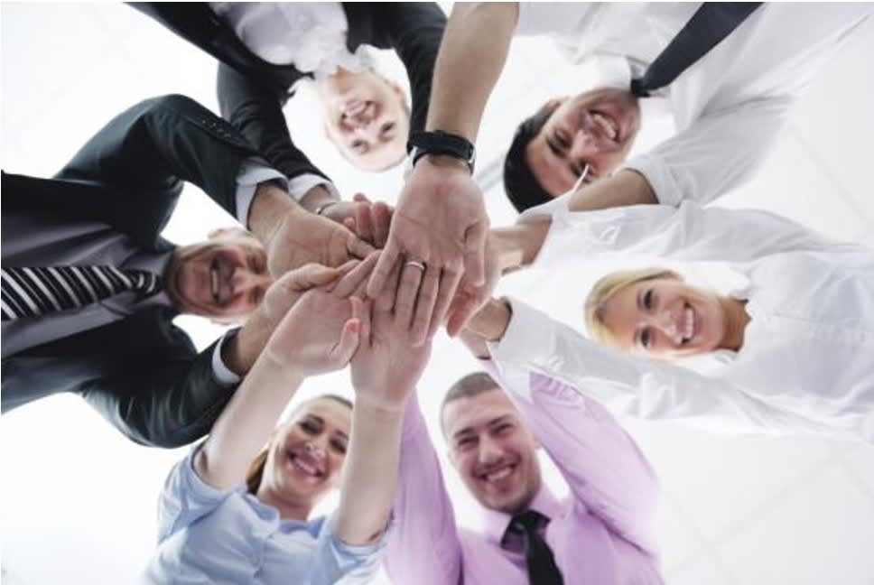 A group of people placing their hands together in circle, symbolizing a gesture of collaboration and support.
