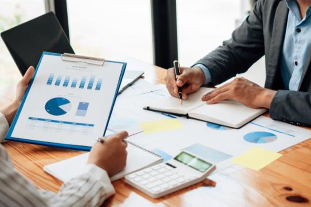 Two professionals reviewing financial charts and graphs during a business meeting, with documents, a notebook, and a calculator on the desk.
