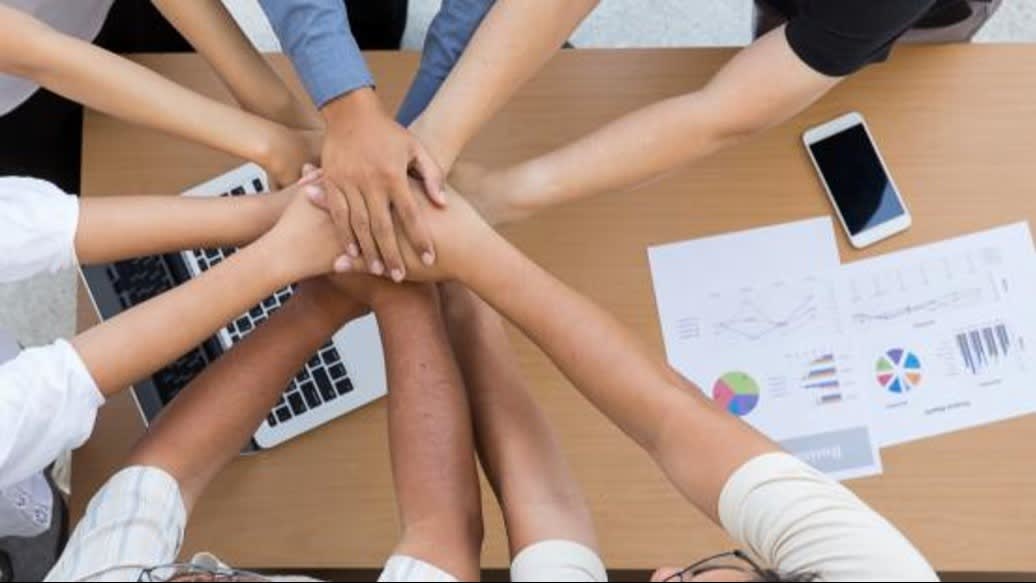 Multicultural team stacking hands to represent teamwork, trust, and partnership in a professional setting.
