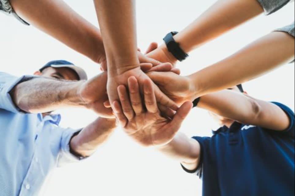 A group of people stacking hands in a circle, symbolizing teamwork, unity, and collaboration.