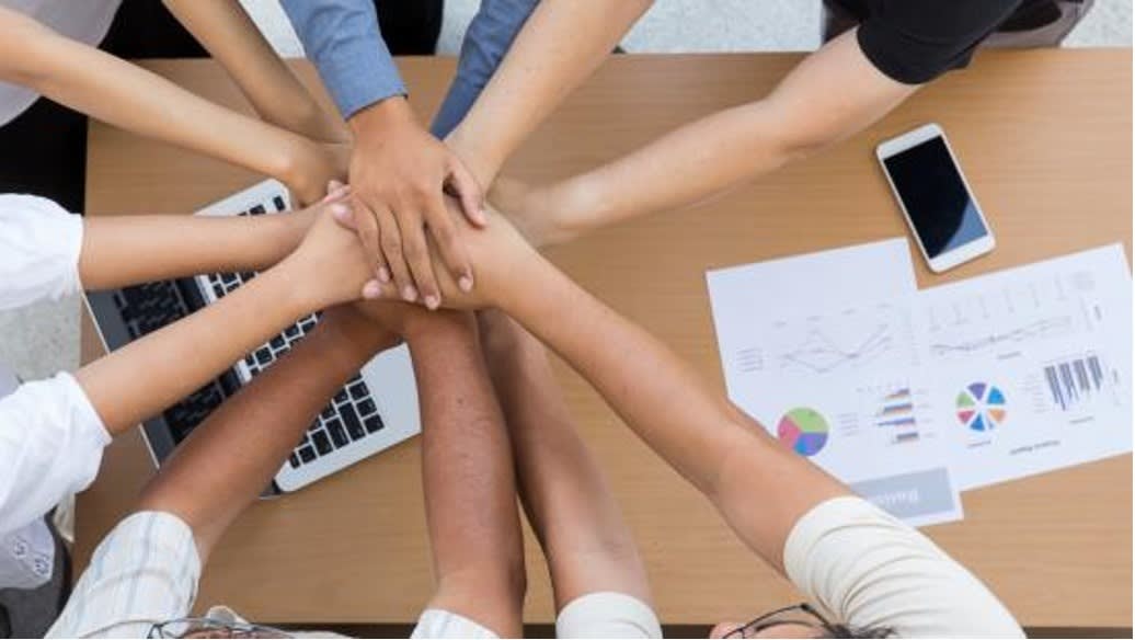 A group of individuals stacking hands in a circle, symbolizing teamwork, collaboration, and collective effort.