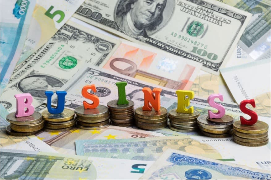 Colorful BUSINESS letters on stacked coins surrounded by international currency notes, symbolizing global finance and business growth.