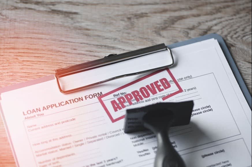 Loan application form with a red "APPROVED" stamp, clipboard, and stamp, symbolizing loan approval and financial success.
