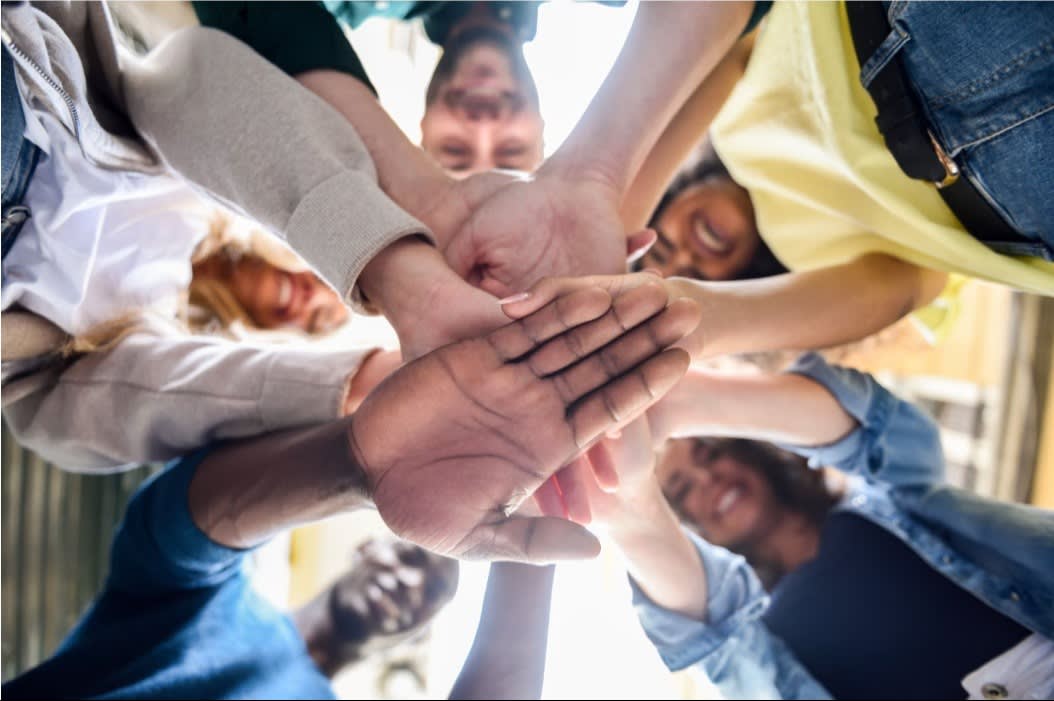 A group of people stacking hands in a circle, symbolizing teamwork, unity, and collaboration.