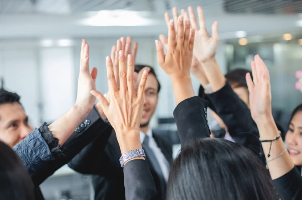 A group of business professionals giving a collective high-five, symbolizing teamwork, success, and unity.