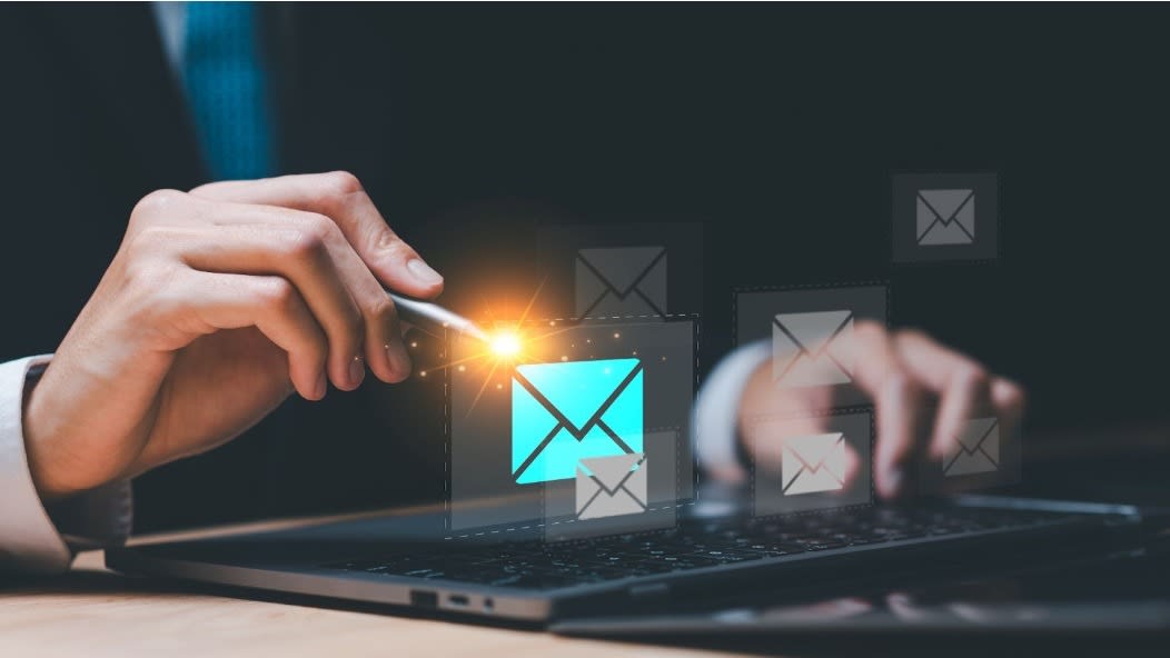 A person interacting with a glowing email icon on a digital interface while using a laptop, symbolizing email communication and digital marketing.