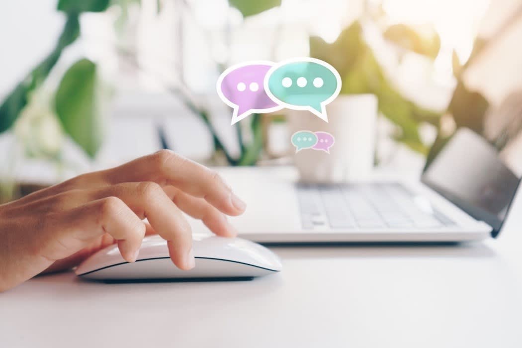 A hand using a mouse near a laptop with chat icons hovering above, representing online messaging or real-time communication.