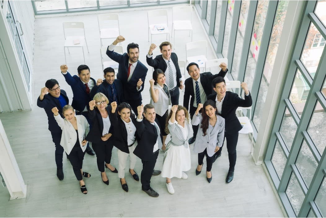 A diverse group of business professionals raising their fists in celebration in a modern office, symbolizing teamwork, success, and unity.