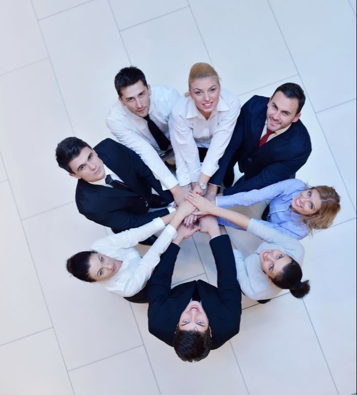 A group of business professionals stacking their hands in a circle, symbolizing teamwork, unity, and collaboration in a corporate setting.