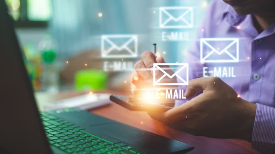 A person using a stylus on a smartphone with glowing email icons and a laptop nearby, symbolizing email communication and digital marketing.