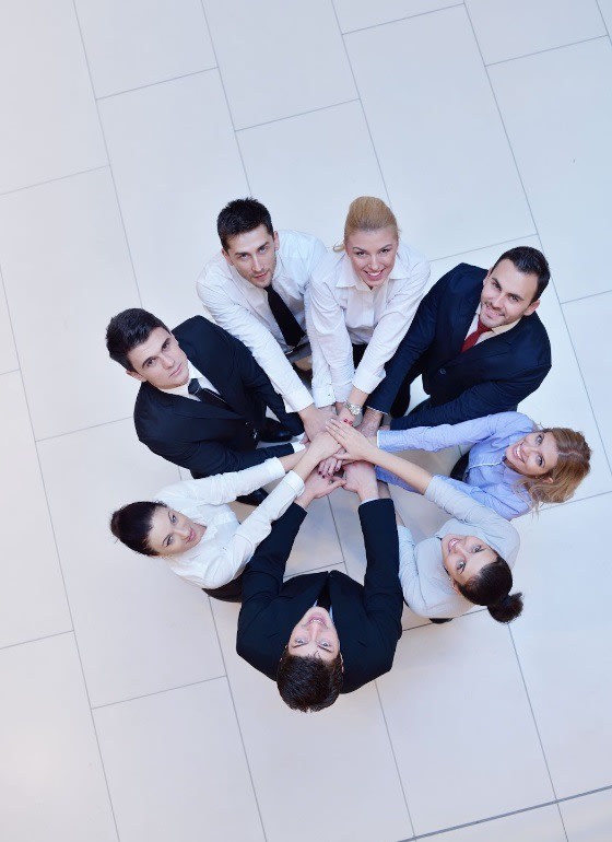 A group of business people standing in a circle with hands joined in the center, symbolizing teamwork and unity in a professional environment.