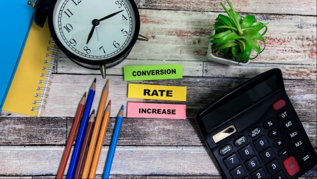 Flat lay of a desk with a clock, pencils, calculator, plant, and sticky notes that read "Conversion Rate Increase," suggesting a focus on improving metrics.