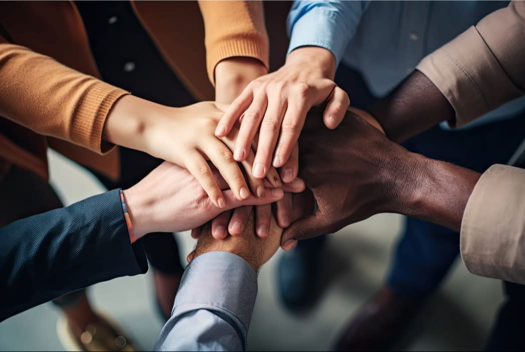 A close-up of a diverse group of hands stacked together, symbolizing teamwork, unity, and collaboration.
