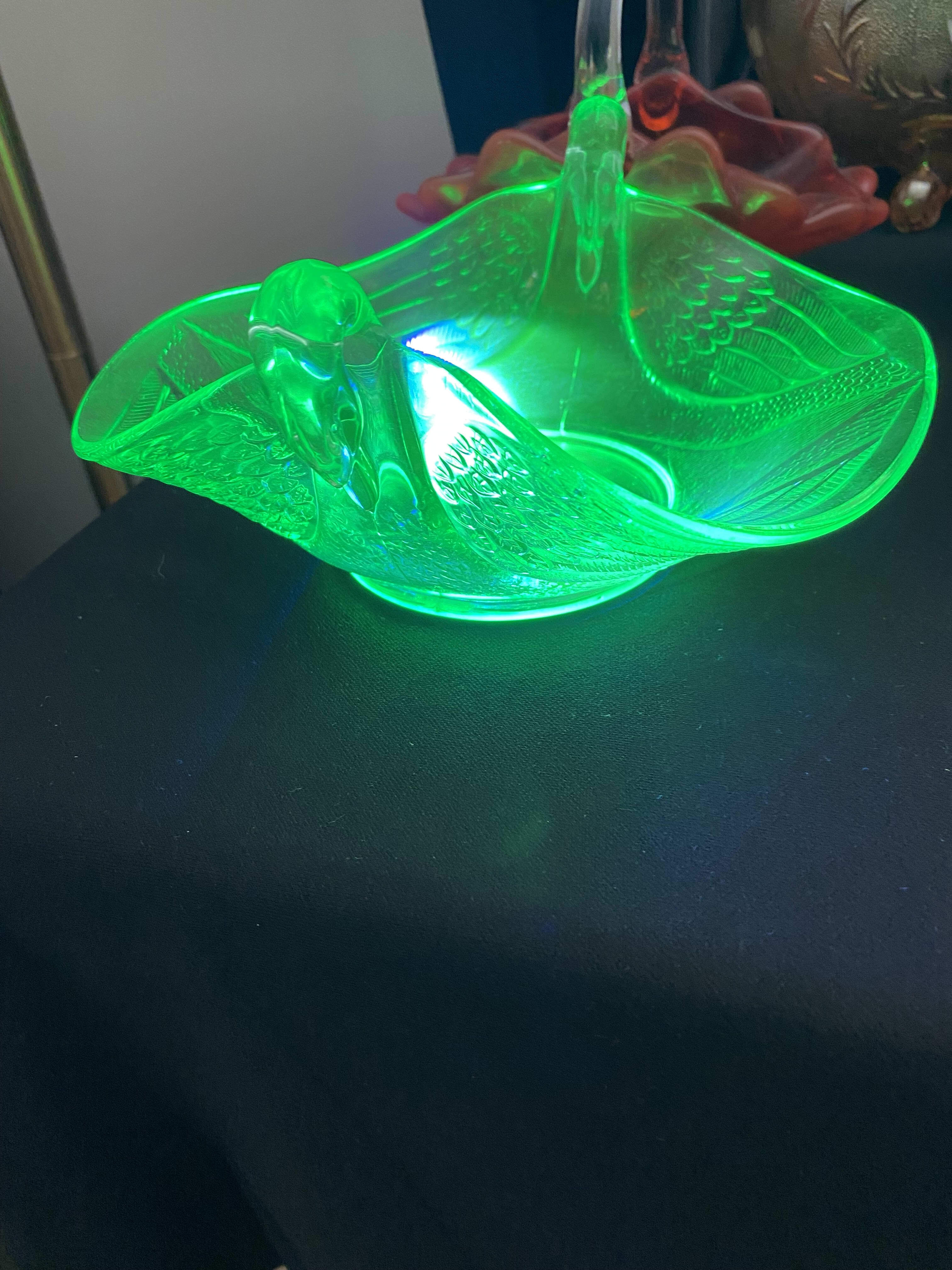 Green uranium glass swan dish glowing bright under a blacklight at an estate sale