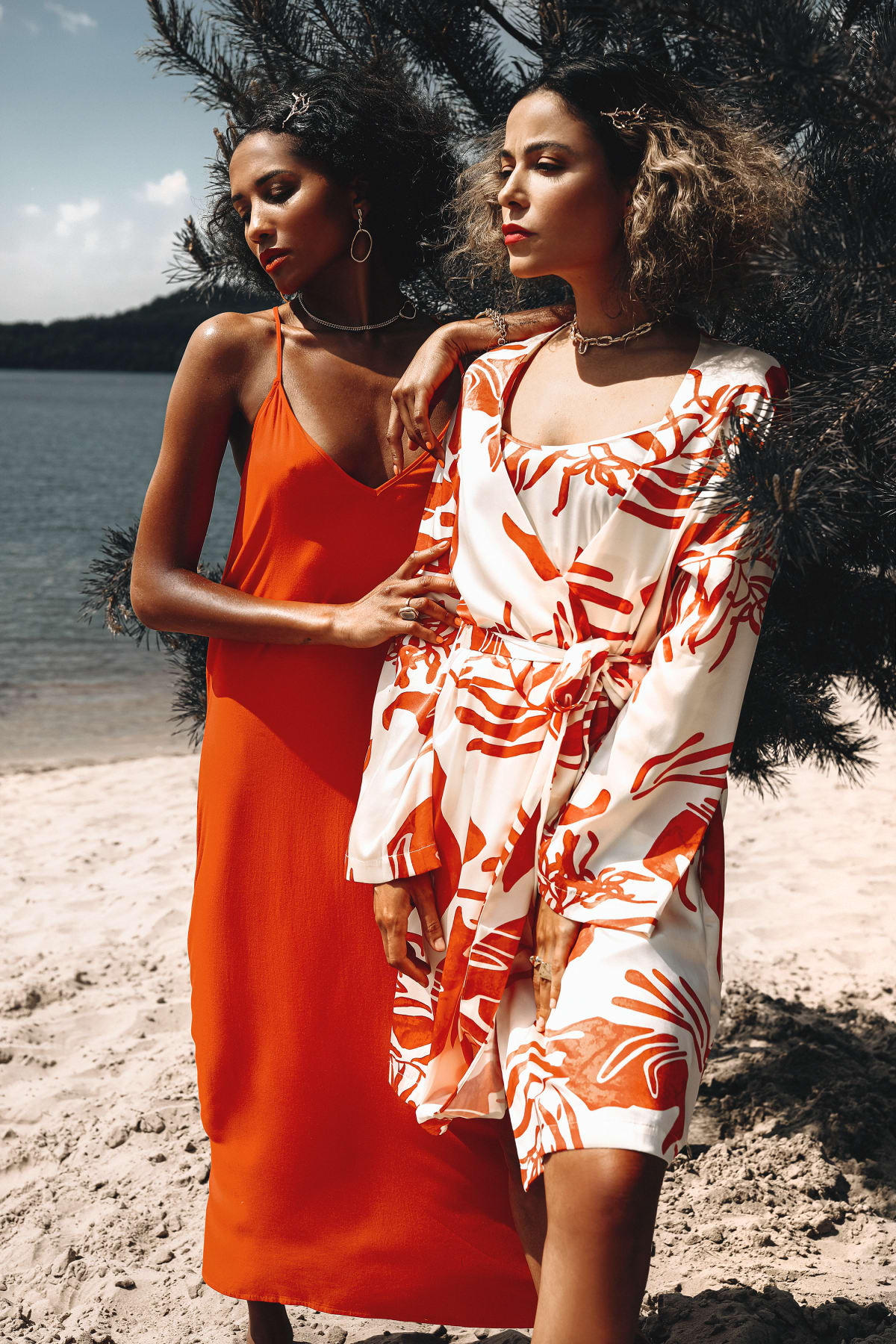 Twee modellen in oranje en wit gedessineerde outfits op het strand, editorial shoot